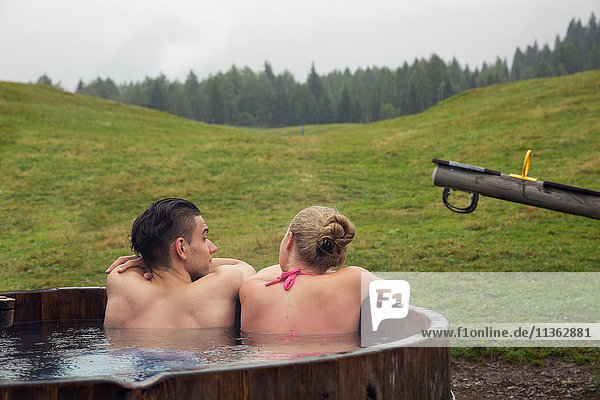 Rückansicht eines jungen Paares beim Entspannen im ländlichen Whirlpool  Sattelbergalm  Tirol  Österreich