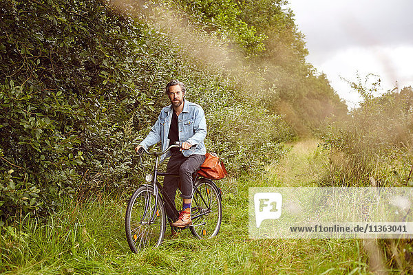 Porträt eines mittelgroßen erwachsenen Mannes auf dem Fahrrad auf einem Feldweg