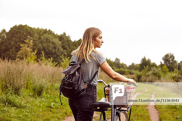 Junge Frau mit Fahrrad  die vom ländlichen Feldweg aus über ihre Schulter schaut