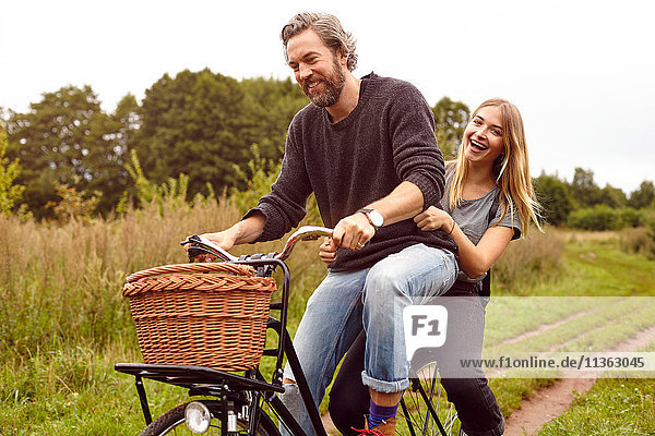 Porträt eines lachenden Paares beim Fahrradfahren auf ländlichem Feldweg