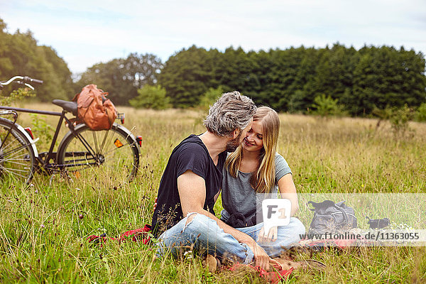 Romantisches Paar sitzt auf einer Picknickdecke auf einem ländlichen Feld