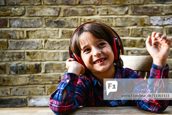 Glücklicher Junge sitzt am Tisch und hört Kopfhörer