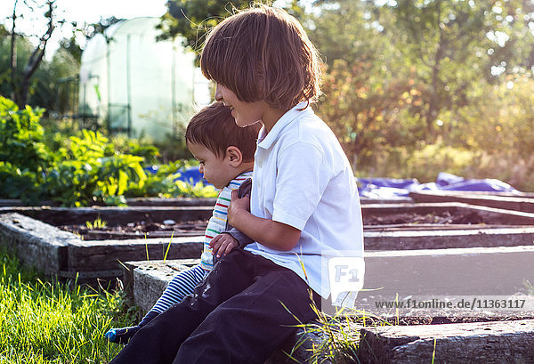 Boy and his baby brother sitting together in sunlit rural garden
