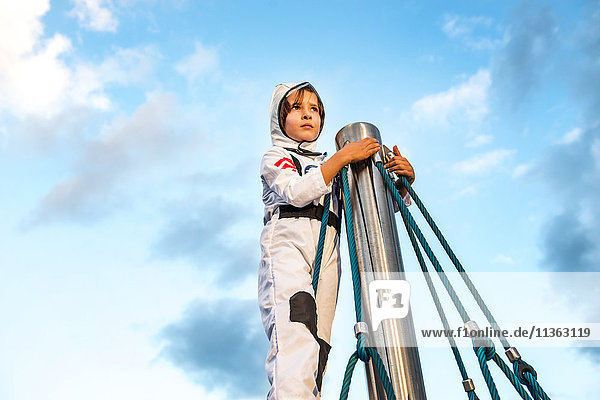 Junge im Astronautenkostüm  der von der Spitze des Klettergerüsts herausschaut