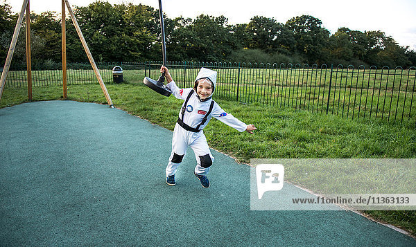 Porträt eines Jungen im Astronautenkostüm  der am Seilzug auf dem Spielplatz zieht