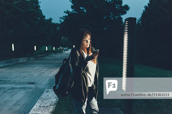 Junge Frau beim Lesen von Smartphone-Texten im Park bei Nacht