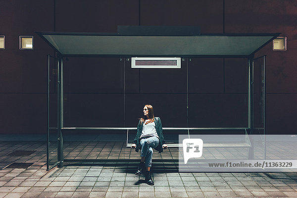 Junge Frau sitzt nachts an der Bushaltestelle