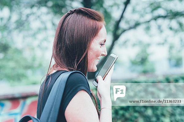 Junge Frau im Gespräch mit Smartphone im Park