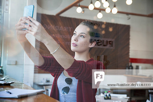 Junge Frau sitzt im Cafe  nimmt Selfie  benutzt Smartphone