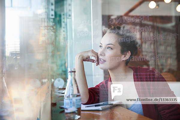 Junge Frau sitzt im Café und schaut aus dem Fenster