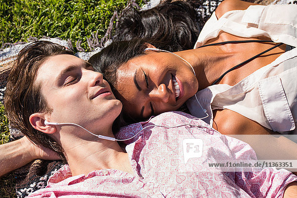 Junges Paar entspannt sich im Freien  liegt auf einer Decke im Gras und teilt sich Kopfhörer
