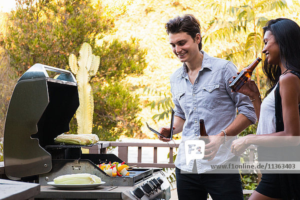Junges Paar im Freien  Bierflaschen haltend  Essen auf dem Grill kochend
