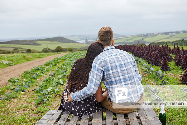 Ehepaar in ländlicher Umgebung sitzt auf Paletten und schaut weg