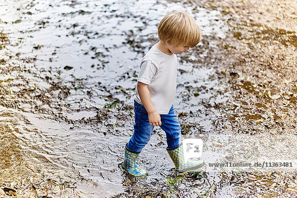 Boy wearing rubber boots playing in muddy puddle