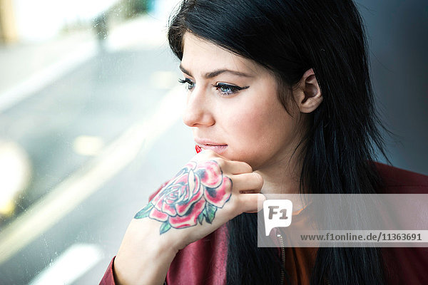 Junge Frau mit Tätowierung auf der Hand  die durch ein Fenster schaut