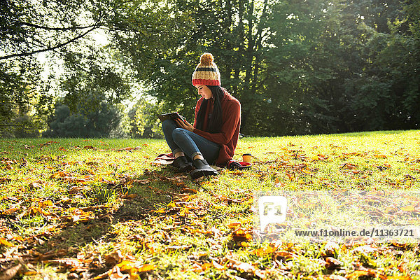 Junge Frau sitzt auf Gras im Park und studiert