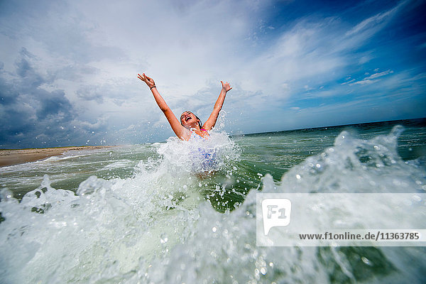 Mädchen springt vor Freude in der Meereswelle
