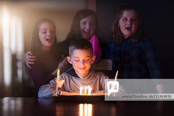 Boy surrounded by friends looking at birthday cake smiling