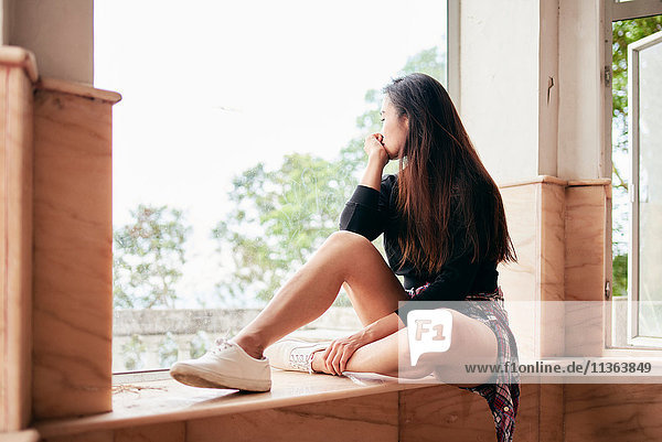 Junge Frau blickt vom Fensterbrett des verlassenen Hauses  Victoria Peak  Hongkong