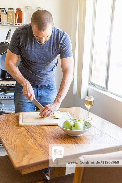 Mittlerer Erwachsener Mann schneidet Apfel am Küchentisch