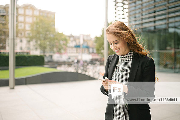 Frau in der Stadt schaut auf Smartphone lächelnd