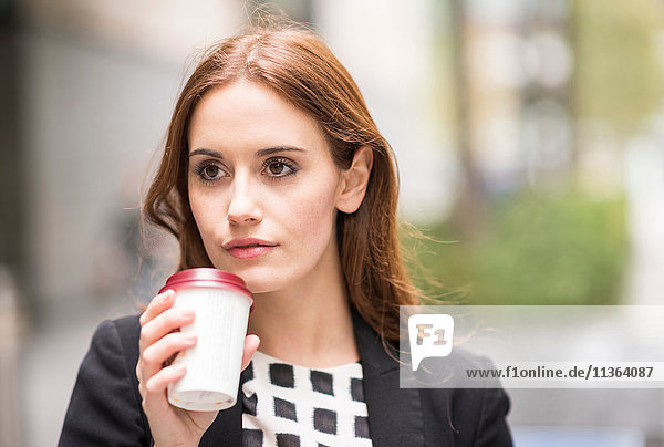 Portrait of woman holding disposable coffee cup looking away