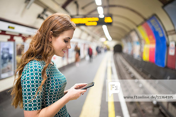 Seitenansicht der Frau auf dem Bahnsteig mit Blick auf das Smartphone