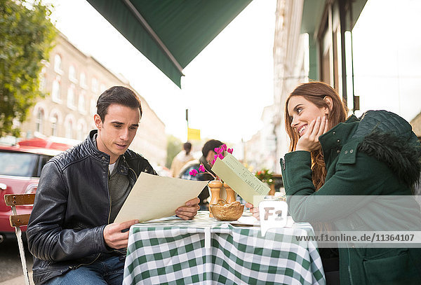 Paar im Straßencafé mit lächelndem Blick auf die Speisekarte
