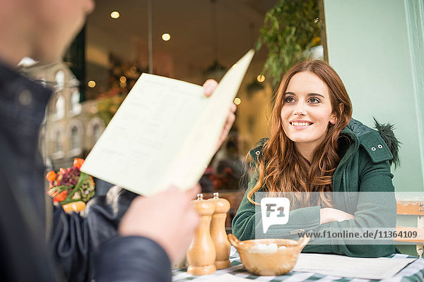 Couple at pavement cafe looking at menu smiling