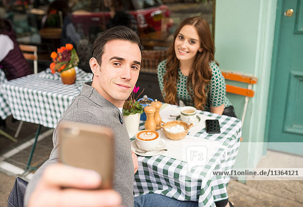 Couple at pavement cafe talking selfie
