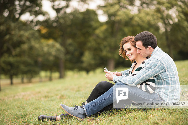 Couple sitting in field hugging looking at smartphone