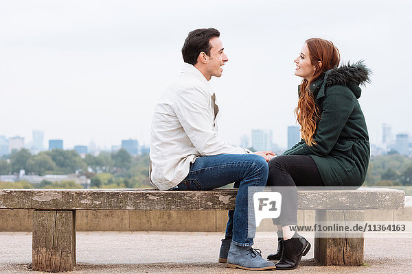 Side view of couple sitting face to face on bench