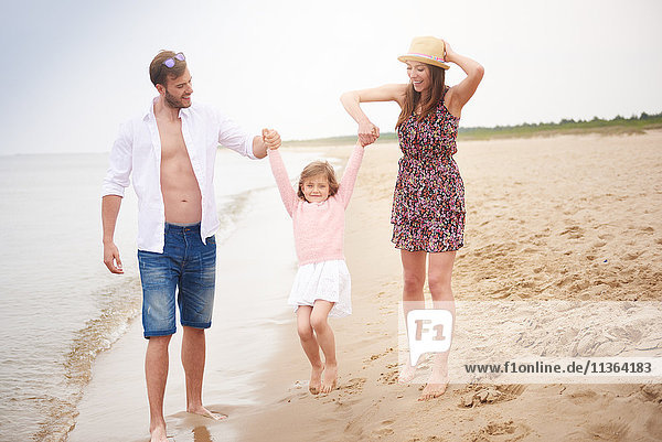 Familie geht am Strand spazieren und schwingt die Tochter mit der Hand