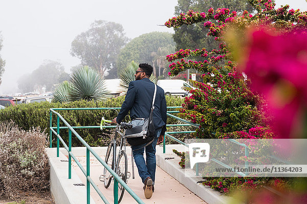 Junger Mann zu Fuß im Freien mit Fahrrad  Rückansicht