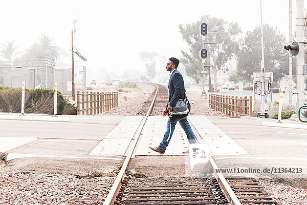 Junger Mann beim Überqueren eines Bahnübergangs  Seitenansicht