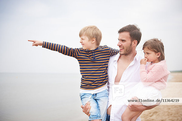 Vater trägt Kinder im Arm am Strand