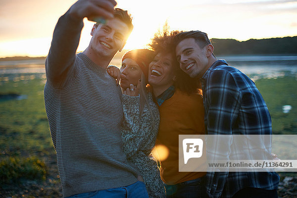 Vier junge Erwachsene nehmen Smartphone-Selfie bei Sonnenuntergang am Meer