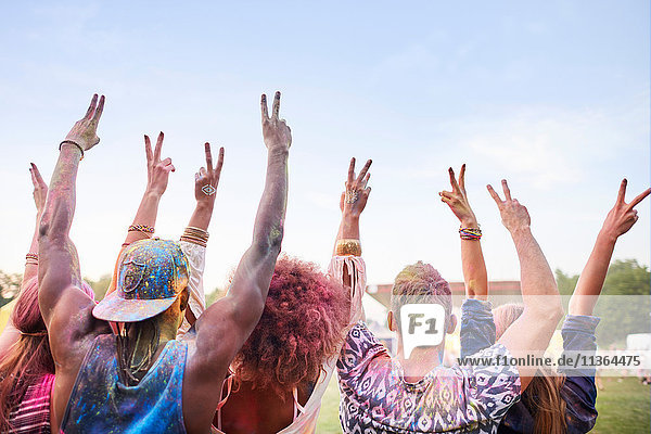 Gruppe von Freunden auf dem Fest  mit bunter Pulverfarbe bedeckt  Arme erhoben  Friedenszeichen mit den Fingern machen  Rückansicht