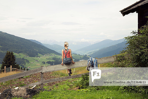 Rückansicht einer auf einem Zaun sitzenden Frau mit Blick auf die Berglandschaft  Sattelbergalm  Tirol  Österreich