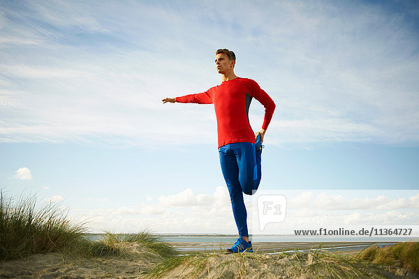 Man on sand dune standing on one leg doing stretching exercises