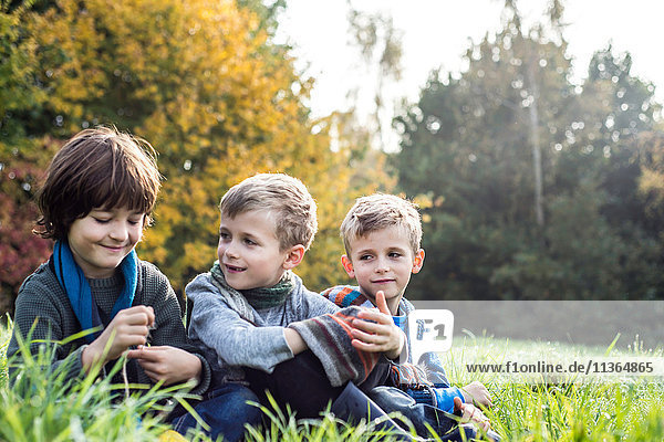 Three boys  sitting together in field  in autumn