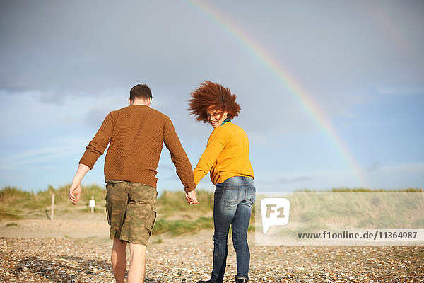 Couple walking on beach towards rainbow