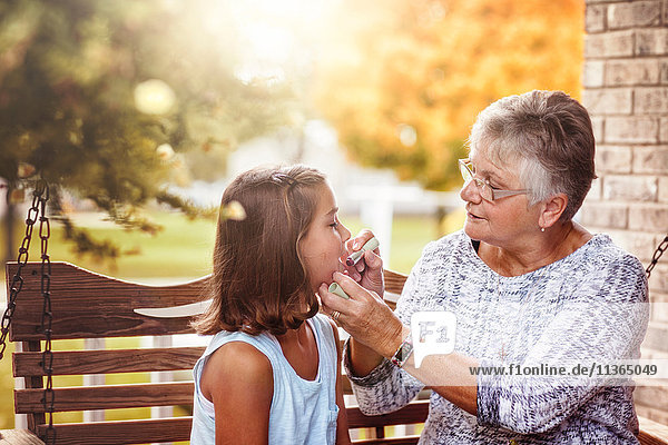 Großmutter und Enkelin sitzen auf der Verandaschaukel  Großmutter zeigt der Enkelin  wie man Lippenstift aufträgt