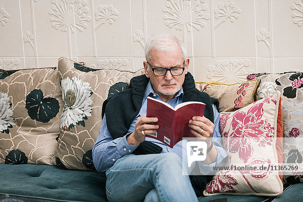 Älterer Mann liest Buch auf Couch