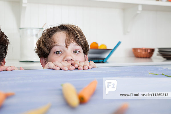 Young boy peering over kitchen work surface