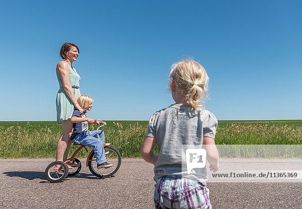 Mutter und Kinder fahren Dreirad in ländlicher Gegend