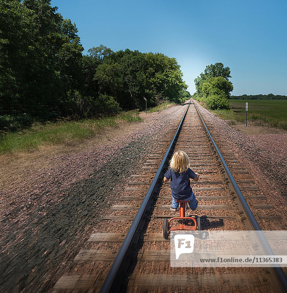 Rückansicht eines Jungen auf einem Dreirad auf einer Eisenbahnstrecke