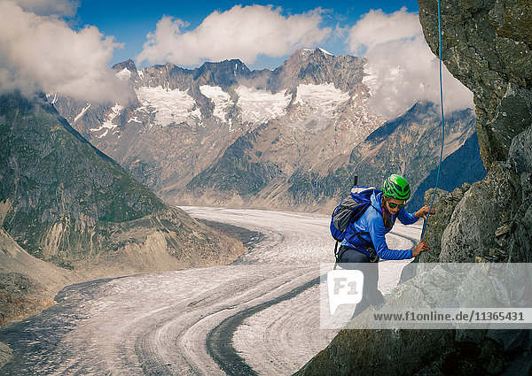 Female climber climbing rock face over Aletsch Glacier Canton Wallis Switzerland