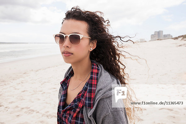 Young woman in sunglasses strolling alone on windy beach  Western Cape  South Africa