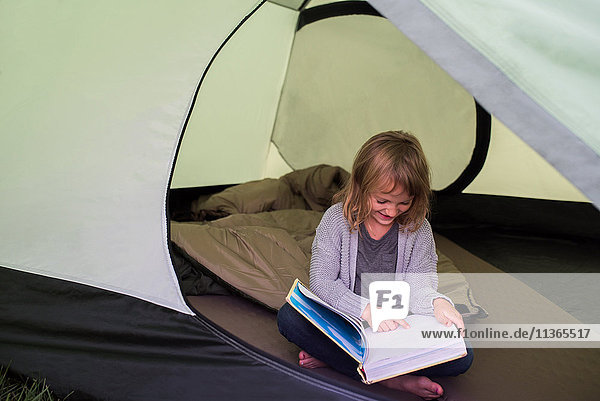 Junges Mädchen sitzt im Zelt und liest ein Buch